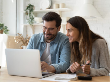 Happy-couple-looking-at-laptop-computer-and-discussing-finances-together