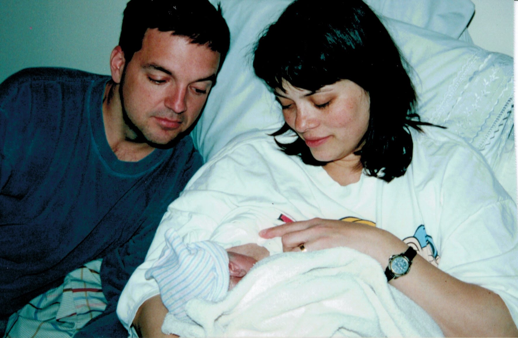 woman nursing newborn while her husband gazes at the baby 
