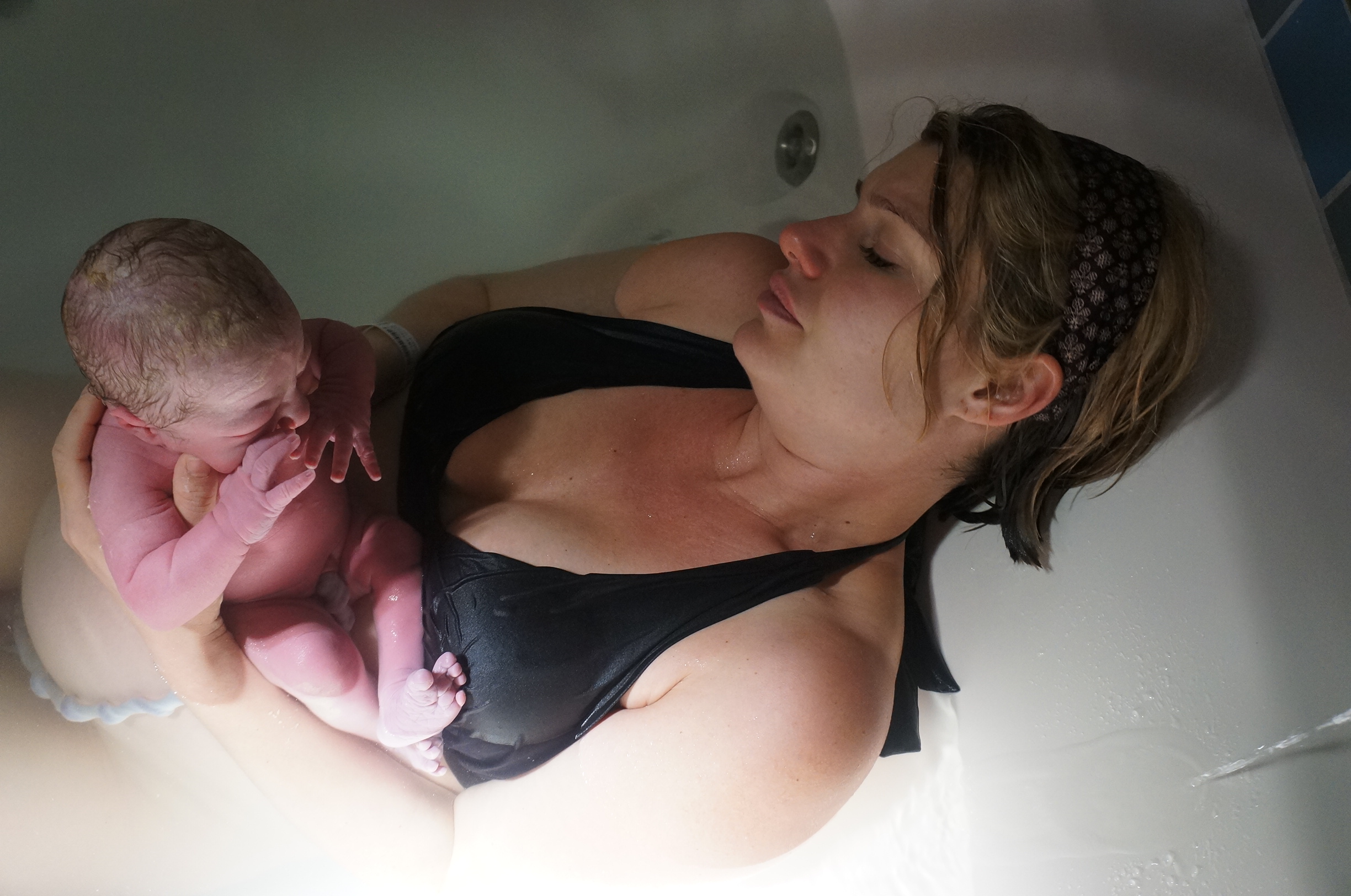 Woman holding baby in waterbirth tub she delivered in
