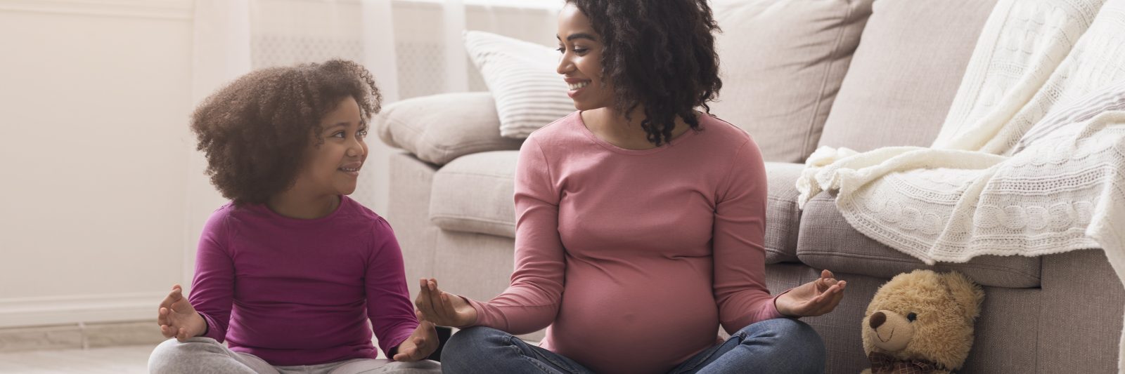 Pregnant-black-mother-and-her-little-daughter-practicing-yoga-at-home