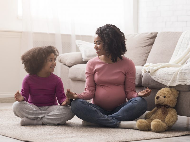 Pregnant-black-mother-and-her-little-daughter-practicing-yoga-at-home