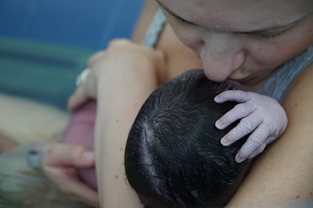 mom holding newborn baby after delivering in waterbirth tub 