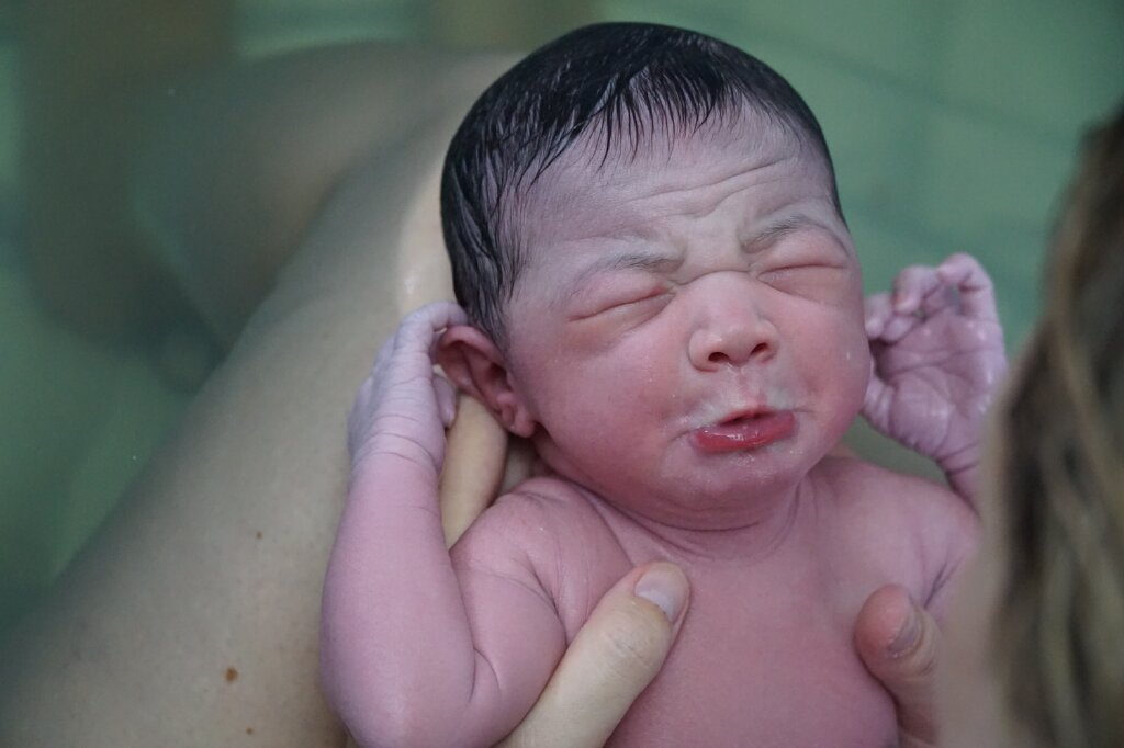 newborn baby resting on mom's legs after being born in a waterbirth tub