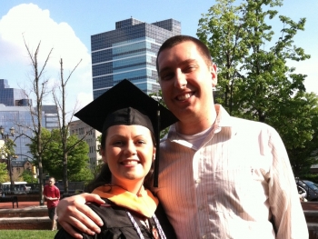 Happy woman in graduation cap and gown standing next to husband