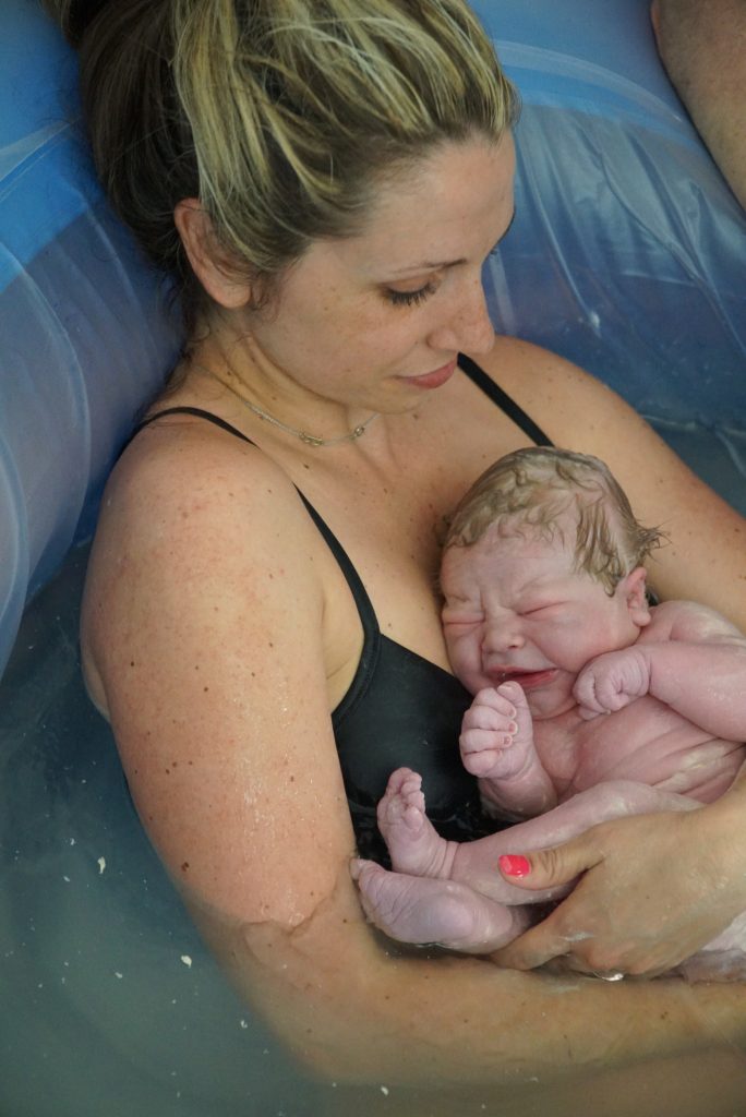 woman holding newborn after giving birth in a birth tub
