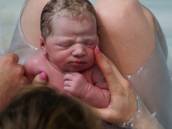 newborn on mom's knees in waterbirth tub midwifery care